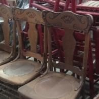 Old wooden chairs with carved backs and worn seats, stacked closely together indoors