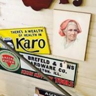 Vintage metal signs and a portrait on a wall, including a yellow Karo sign and a Bredefeld hardware sign.