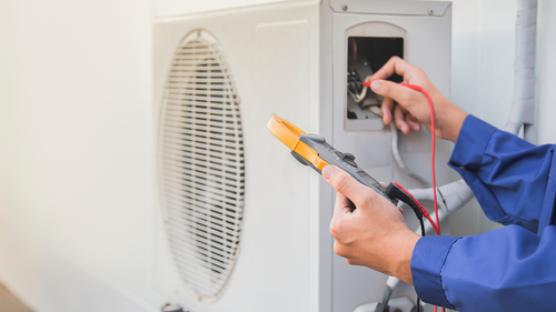 A man is sitting on the ground working on an air conditioner.
