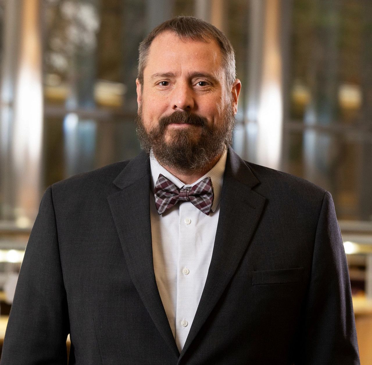 A professional headshot of a person with a beard wearing a dark blazer, light-colored shirt, and a patterned bowtie.