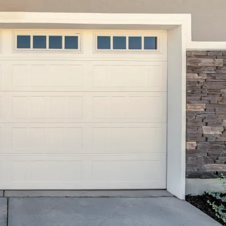 A white garage door with a four-pane window section, set next to a stacked stone wall.