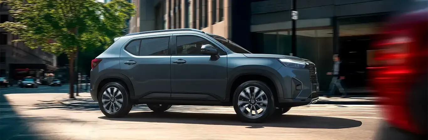 SUV cinza-escuro estacionado em uma rua da cidade com um veículo vermelho desfocado passando em primeiro plano.