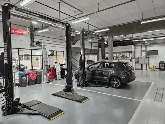 Oficina mecânica com dois elevadores para carros e um SUV preto em uma garagem limpa.
