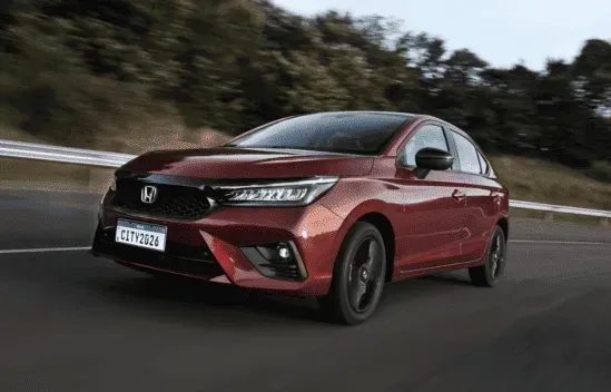 Sedan Honda City vermelho trafegando em uma estrada, com árvores ao fundo.