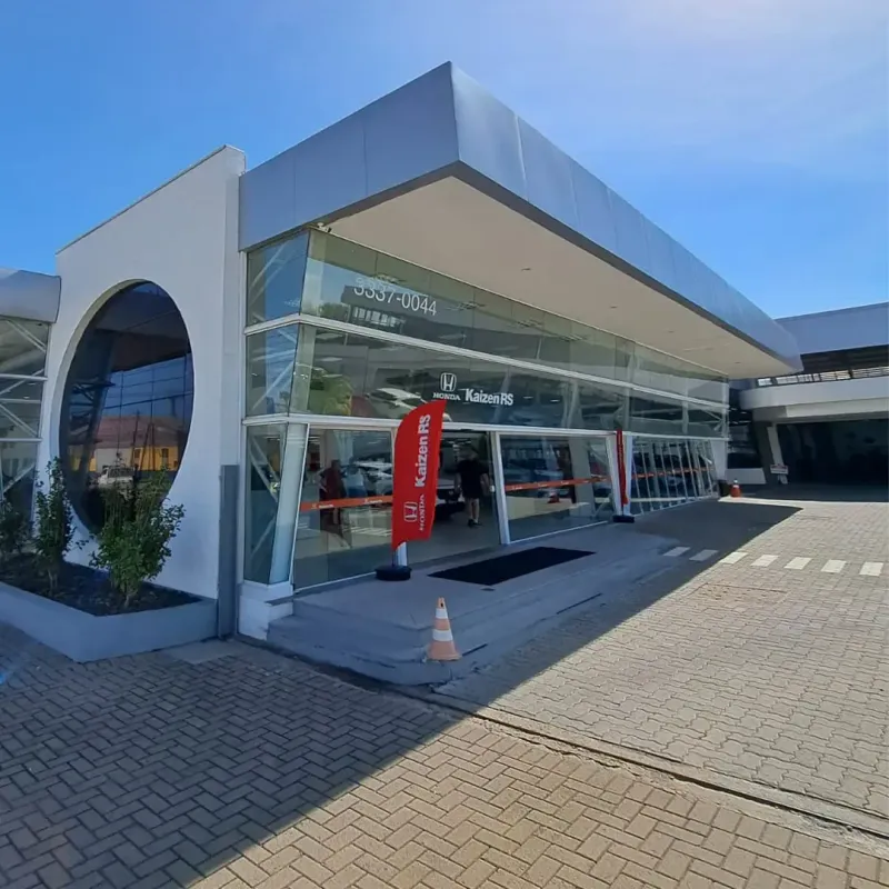 Concessionária de automóveis moderna com janelas de vidro, fachada cinza e branca e uma bandeira vermelha da Toyota.