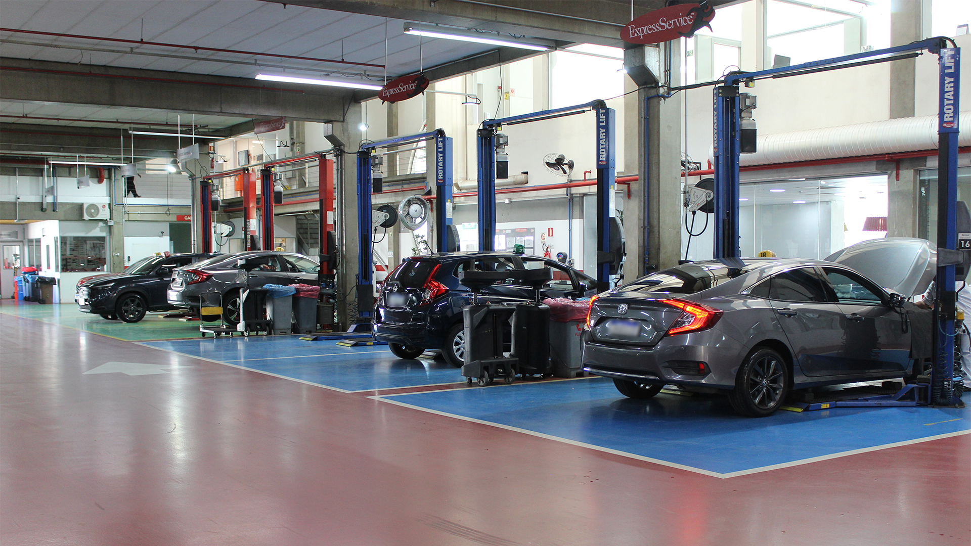 Carros sendo reparados em uma oficina mecânica bem iluminada, com vários veículos em elevadores.