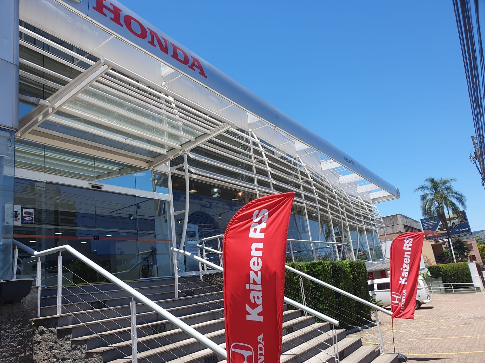 Concessionária Honda com bandeiras vermelhas; céu azul.
