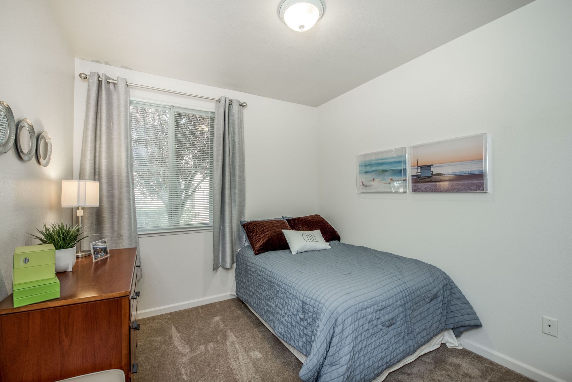 a bedroom with a bed , dresser , lamp and window .