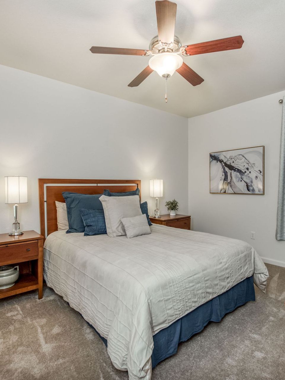 a bedroom with a bed , nightstand , lamp and painting on the wall .