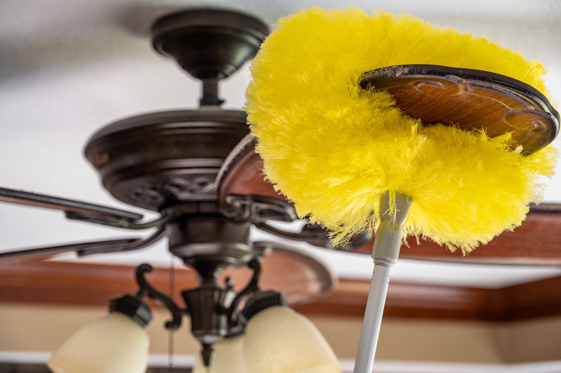 A yellow duster is being used to clean a ceiling fan.