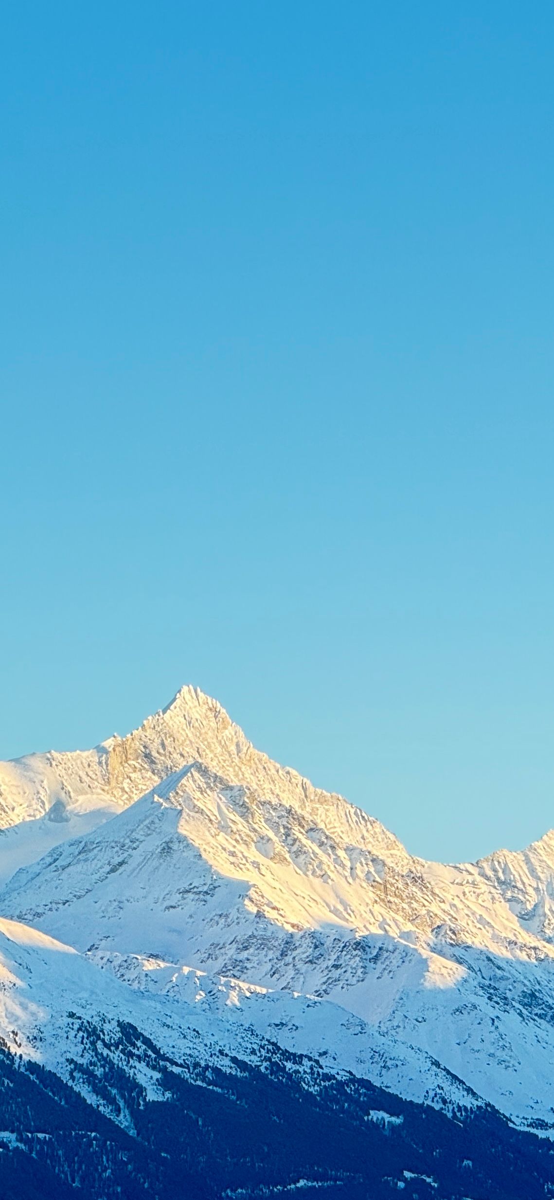 Snow-covered mountain peaks under a clear, bright blue sky.