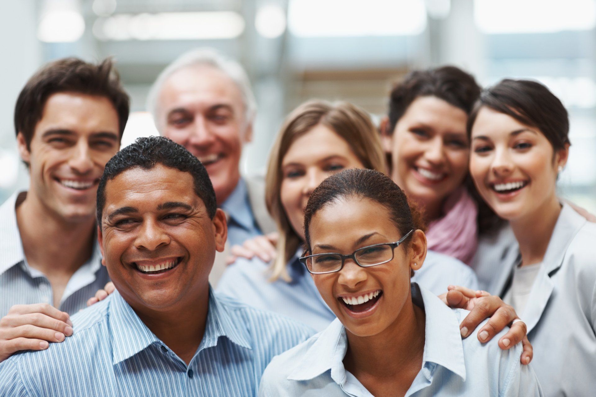 A group of diverse professionals smiling and standing close together in an office setting.