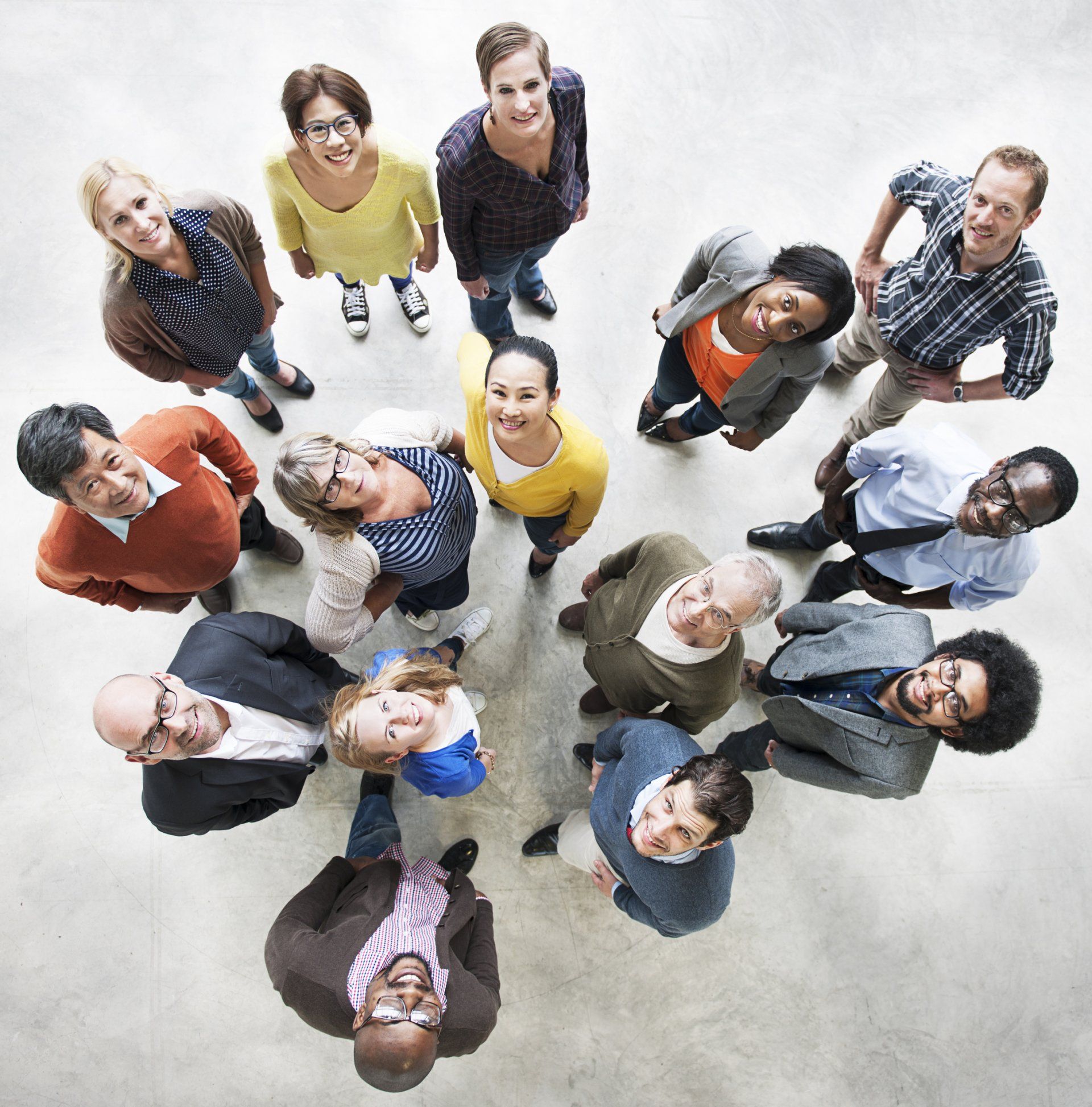 A high-angle view of a diverse group of people standing in a circle, looking up and smiling at the camera.