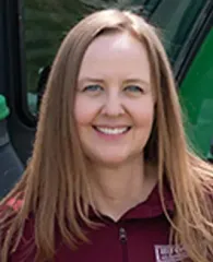 Smiling woman in a maroon top, standing beside a green vehicle
