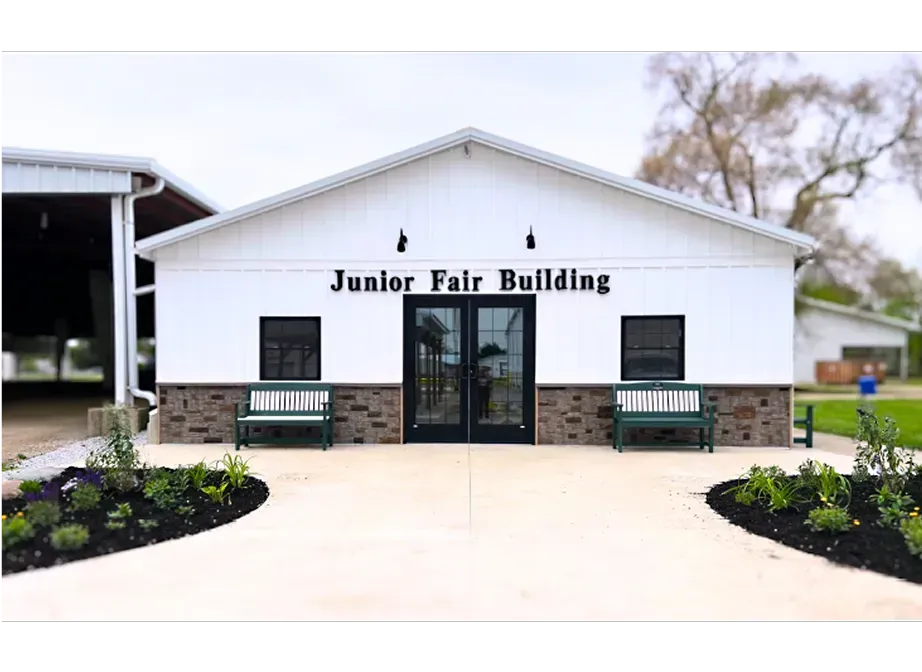 Front view of a white Junior Fair Building with dark trim, glass doors, and flower beds in front