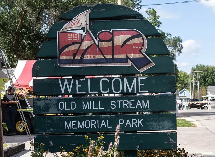Welcome sign for Old Mill Stream Memorial Park with an Airstream logo, painted on a green wood board.