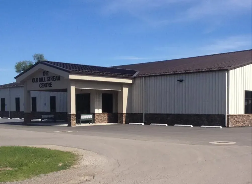 Exterior of a stone-and-metal community center building with a covered entrance under a blue sky