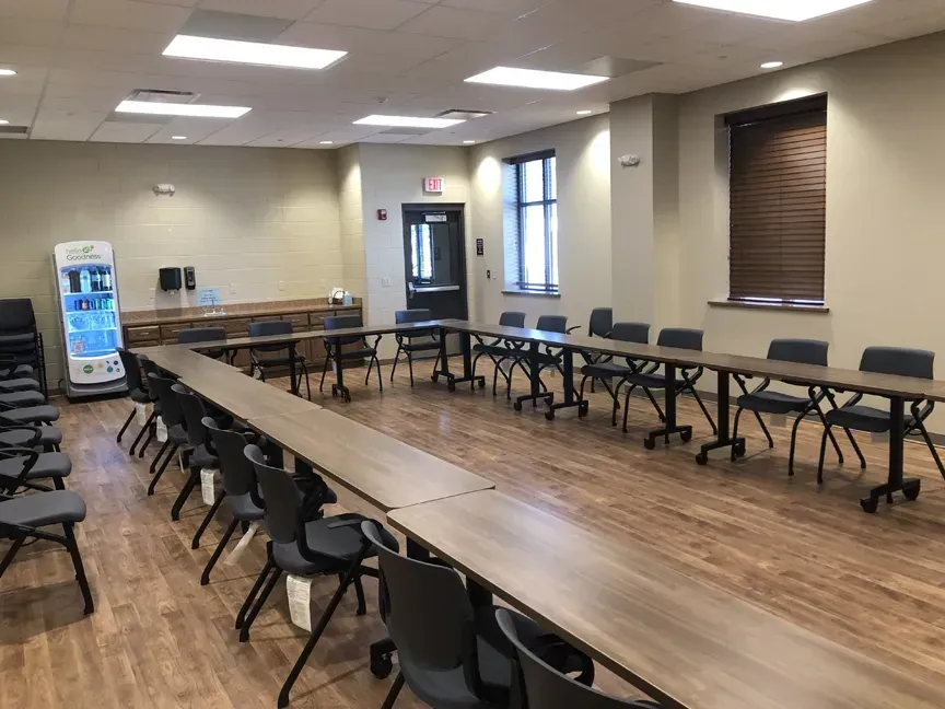 Empty conference room with long U-shaped tables and black chairs on a wood floor