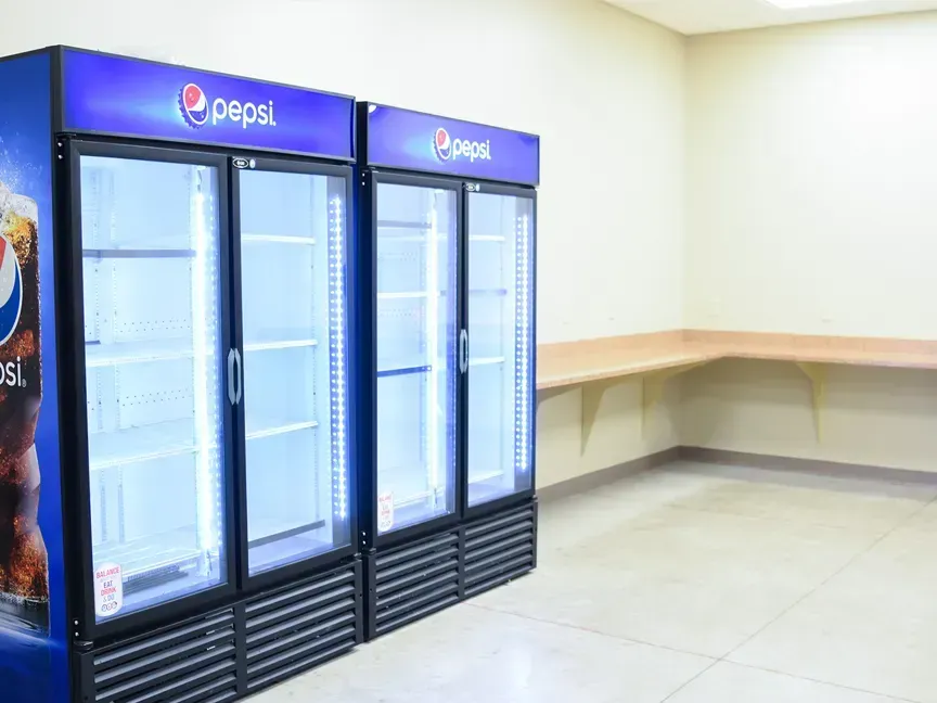 Empty convenience store with Pepsi refrigerators and a long counter against a blank wall.