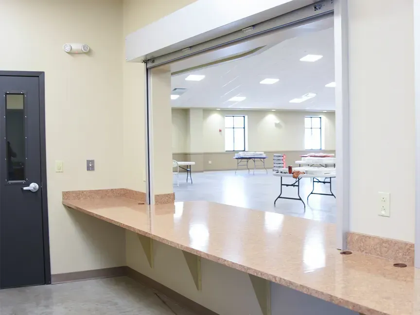 Service counter window overlooking a bright meeting room with tables and chairs