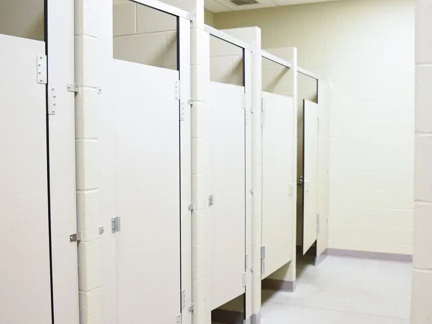 Empty white restroom stalls with open doors in a tiled public bathroom