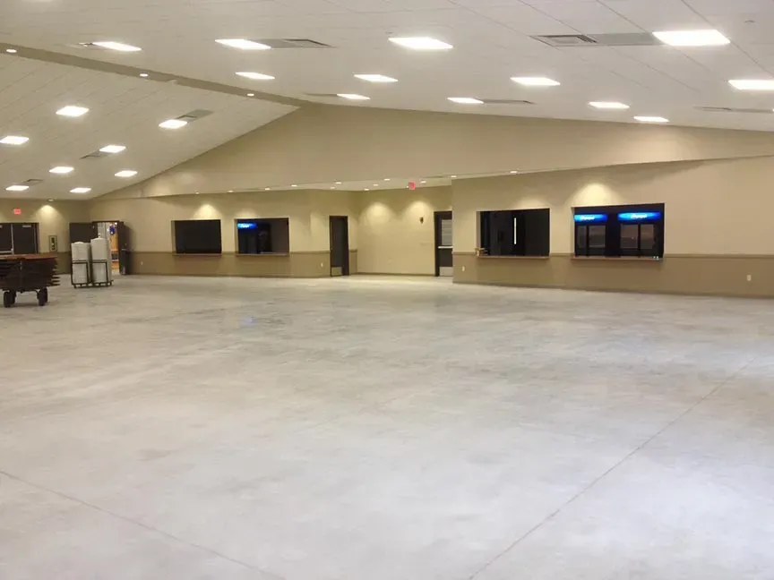 Large empty indoor hall with beige walls, gray floor, and ceiling lights