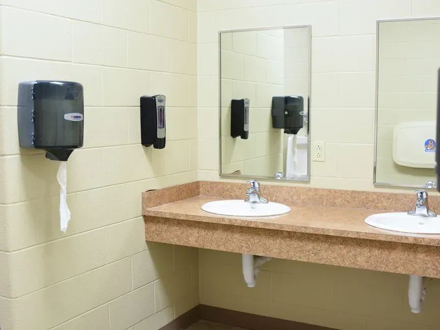 Public restroom sink area with mirrors, soap dispensers, and paper towel dispenser.