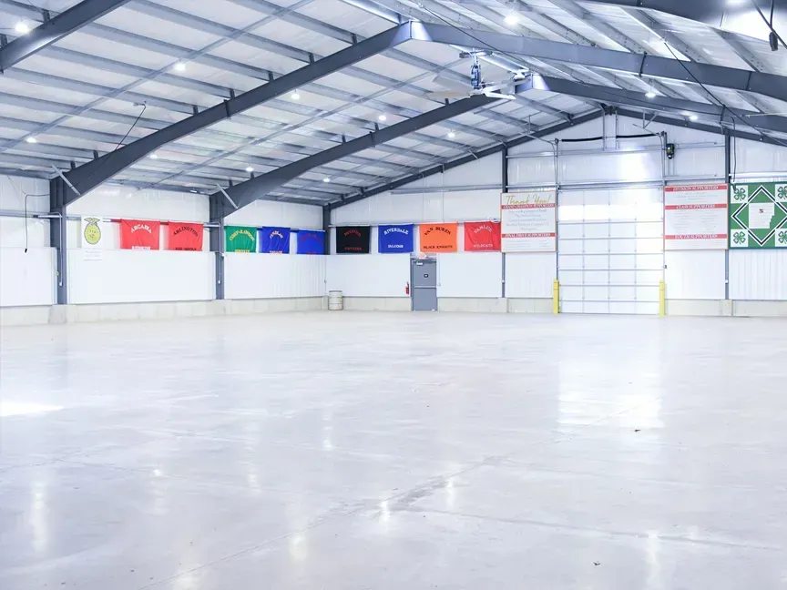 Empty indoor warehouse with high metal ceiling, white floor, and colorful flags along the back wall