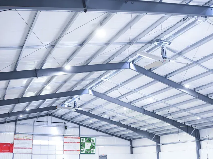 Interior of a steel-framed warehouse roof with white translucent panels and lights, plus a safety sign on the wall