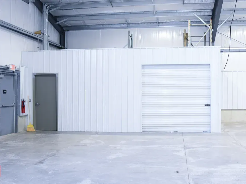 Empty industrial room with white walls, gray door, and a closed roll-up garage door