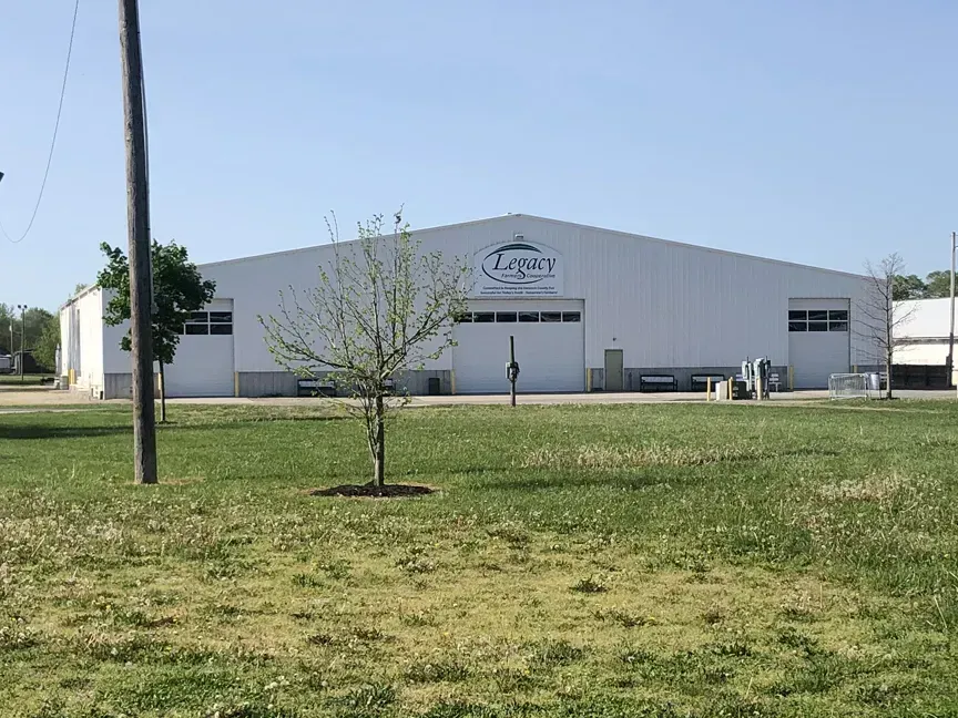 White industrial building with a logo, small trees, and grassy foreground under a clear blue sky