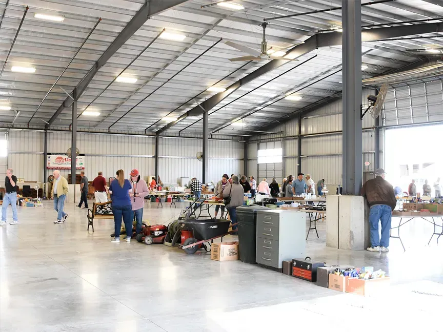 Large indoor warehouse with people gathered around tables and equipment on a polished concrete floor