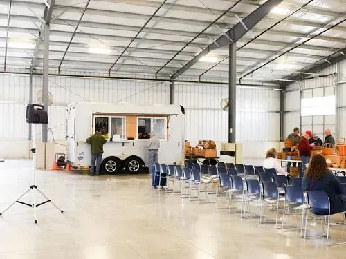 Indoor event hall with rows of blue chairs and a small white concession trailer at the front