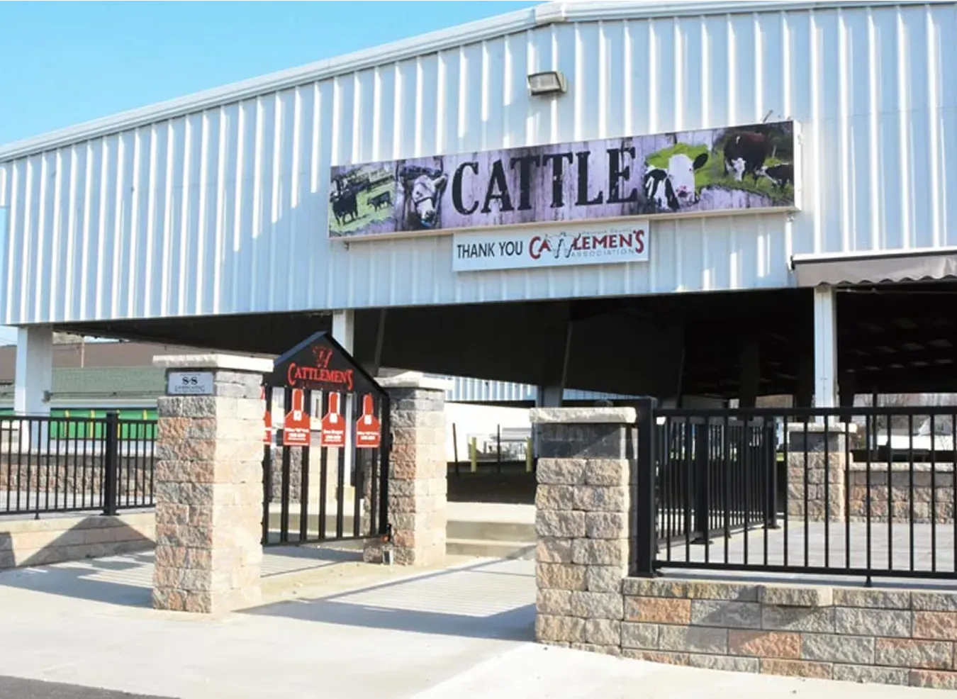 Cattlemanโs restaurant entrance with metal siding, stone gate pillars, and a black fence under a clear sky