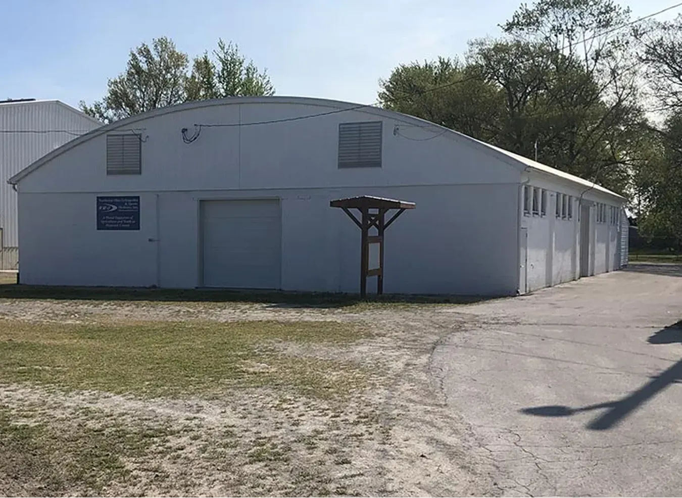 Gray industrial building with garage doors and gravel driveway under a clear sky