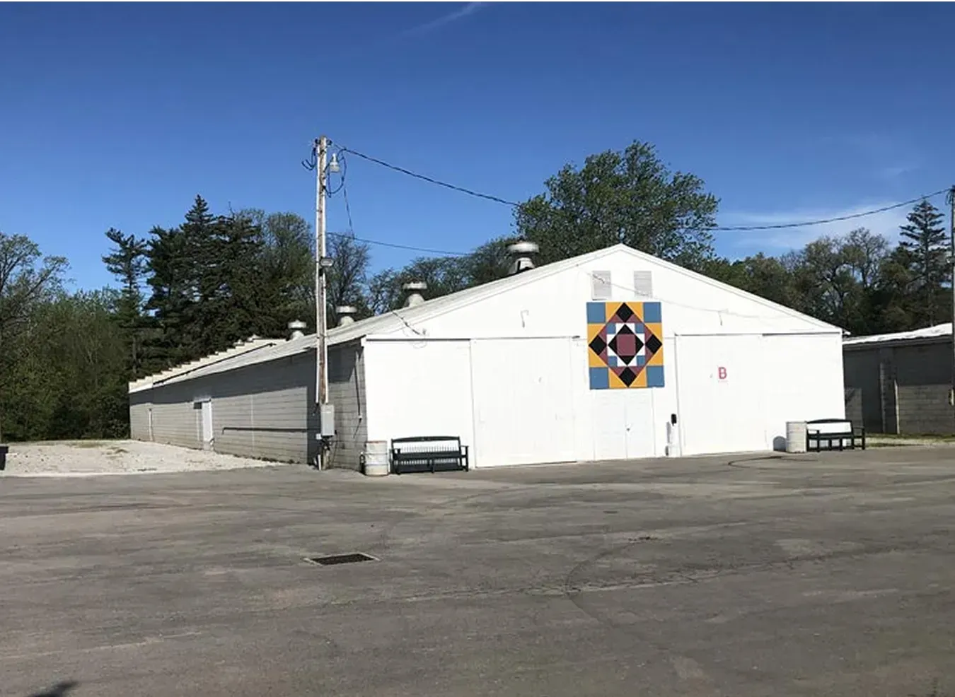 White building with a colorful square mural, large garage doors, and an empty parking lot under a blue sky