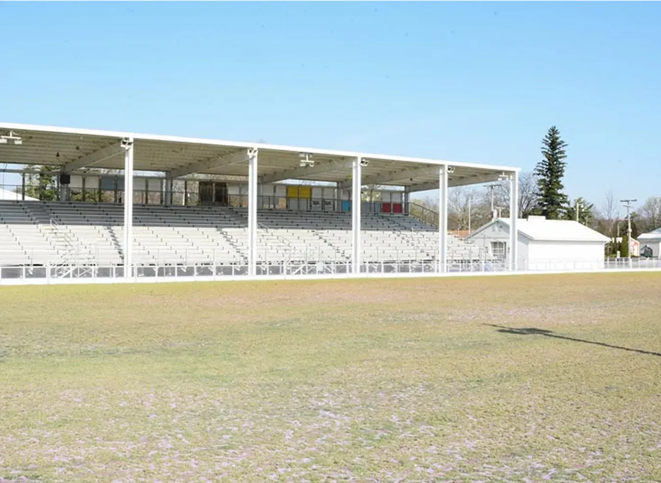 Empty outdoor stadium stand beside a worn grass field under a clear blue sky