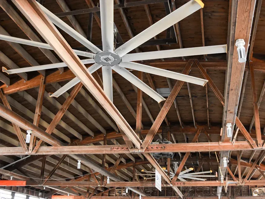 Exposed wooden ceiling beams with large white industrial fans in a warehouse-like space