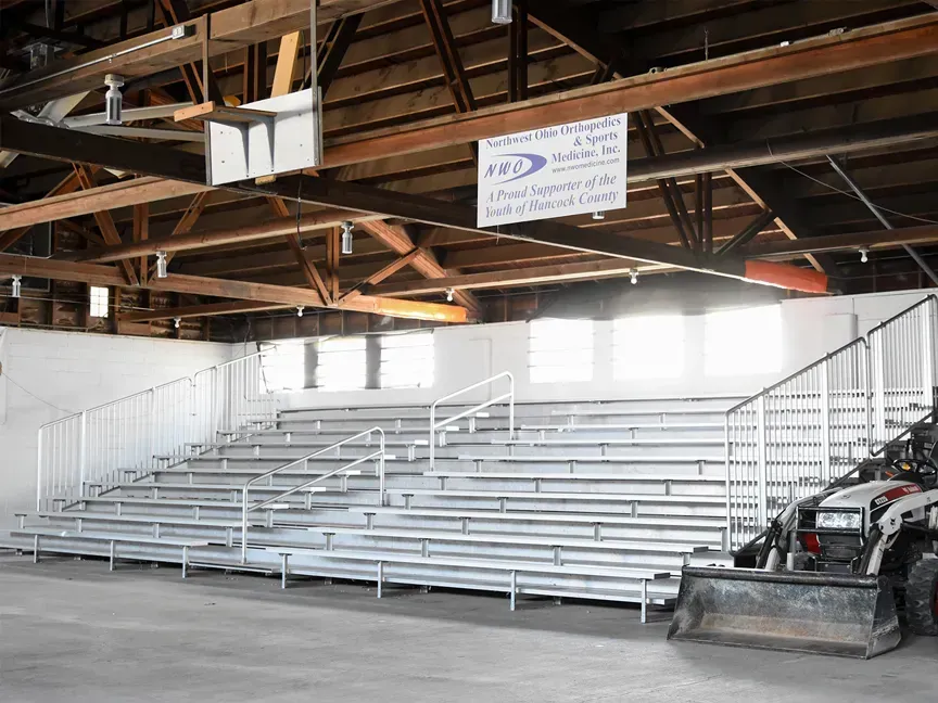 Indoor bleachers in a gym or arena with a wooden roof and white railings