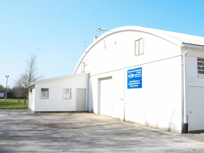 White industrial building with blue sign and garage door beside an empty paved lot under a clear sky