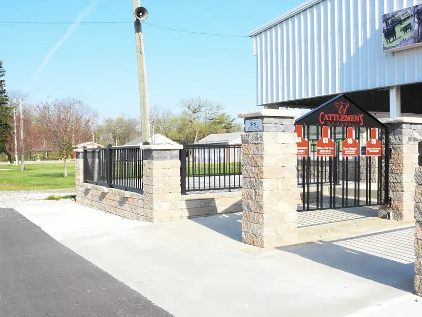 Stone-and-black metal entrance gate beside a building on a sunny street corner