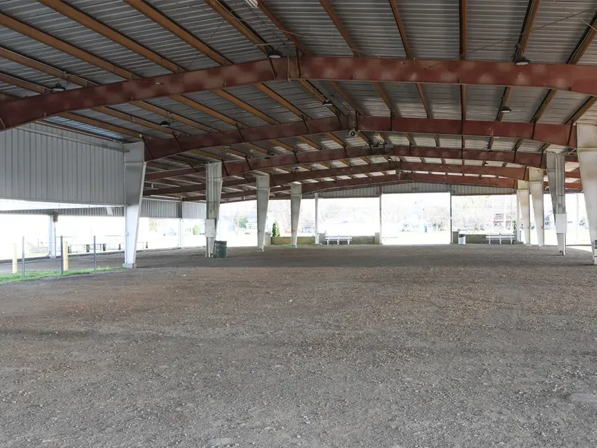 Open-sided metal pavilion with a gravel floor and exposed roof beams, empty inside.