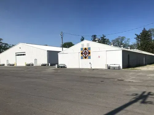 White industrial building with a colorful emblem on the wall, viewed across an empty paved lot under a clear blue sky