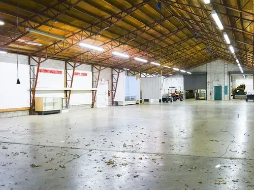 Empty industrial warehouse with a high yellow ceiling and scattered debris on a concrete floor