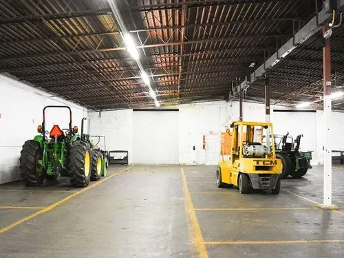 Industrial warehouse with two tractors, one green and one yellow, parked on a concrete floor