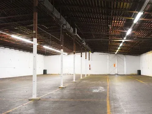 Empty warehouse interior with white walls, concrete floor, and exposed ceiling beams.