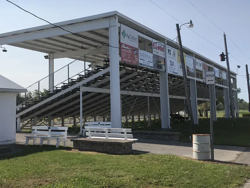 Covered bleachers at a sports field with white benches and advertising banners on the roof