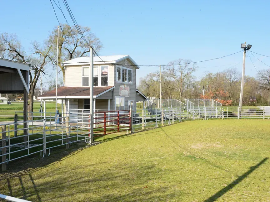 Small white house by fenced grassy track on a sunny day