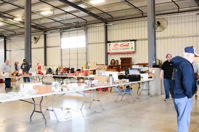 Indoor community hall with folding tables of food and people gathering near a stage backdrop