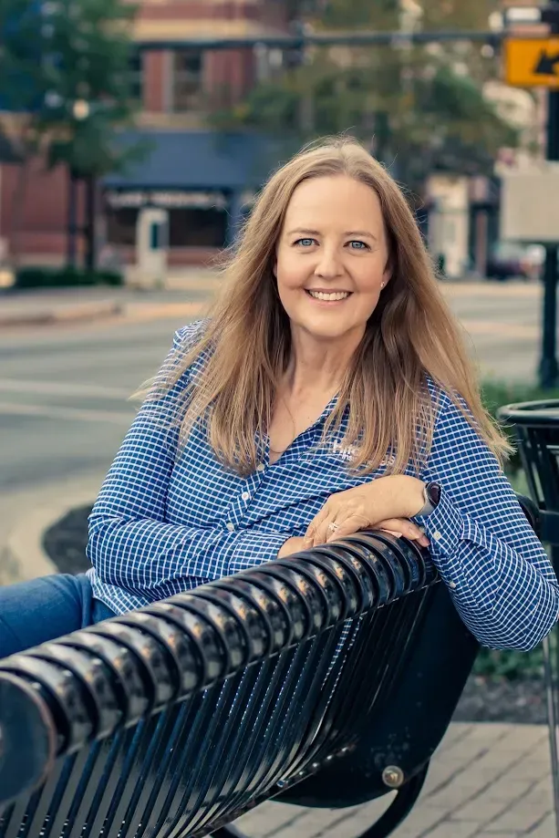Smiling woman in a blue patterned blouse leaning on a black bench on a city sidewalk